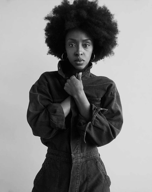 Portrait of an African-American woman with an afro hairstyle wearing a denim jumpsuit against a neutral background in black and white.