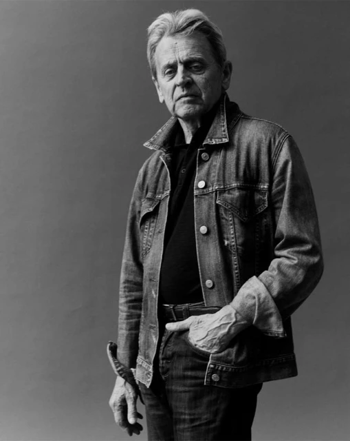 Black and white portrait of a mature adult man in a denim jacket, with a neutral expression, posing in an indoor studio setting.