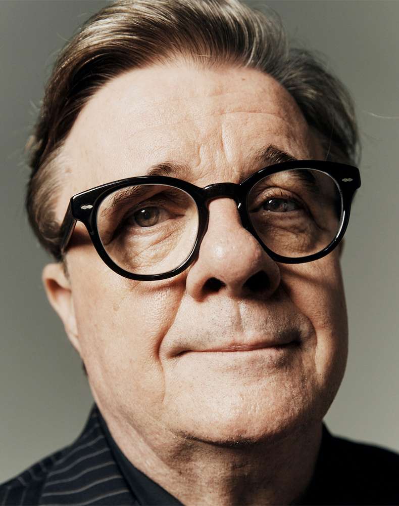 Portrait of an older adult male wearing glasses and a pinstripe shirt against a grey backdrop in a photo studio setting.