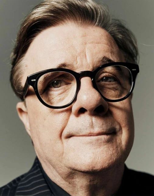 Portrait of an older adult male wearing glasses and a pinstripe shirt against a grey backdrop in a photo studio setting.