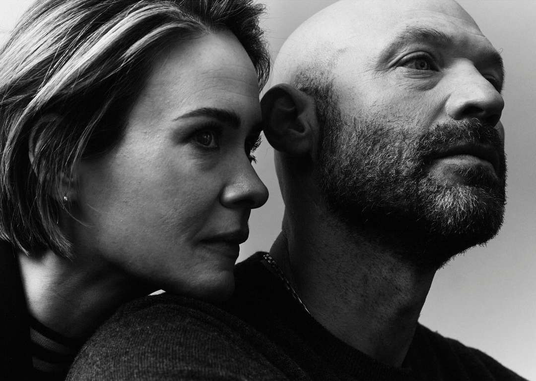 Black and white portrait of a stylish couple in close proximity, featuring an adult woman with short hair and a bald adult male with a beard.