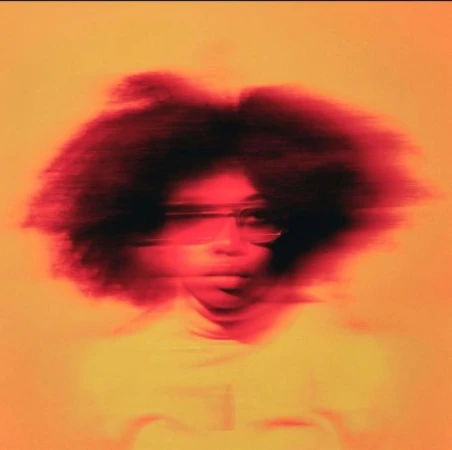 Motion-blurred portrait of a woman wearing glasses against a warm orange background, styled by Tiffani Williams.