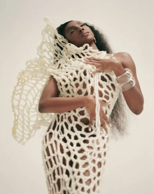 Elegant portrait of a Black woman in a crochet dress with hands on her chest, photographed in a photo studio on a neutral backdrop.