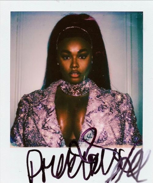 Polaroid portrait of a dark-skinned woman wearing a sparkly blazer, headband, and jeweled choker against a neutral white background.