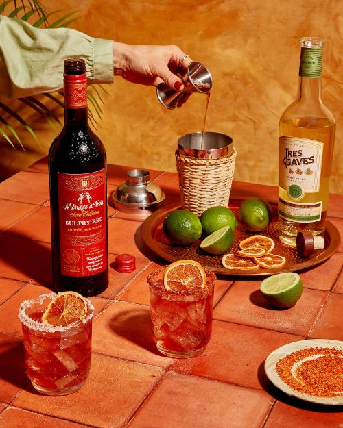 Red wine and tequila cocktail preparation with limes and dried oranges on a terracotta tile surface for food and beverage advertising.