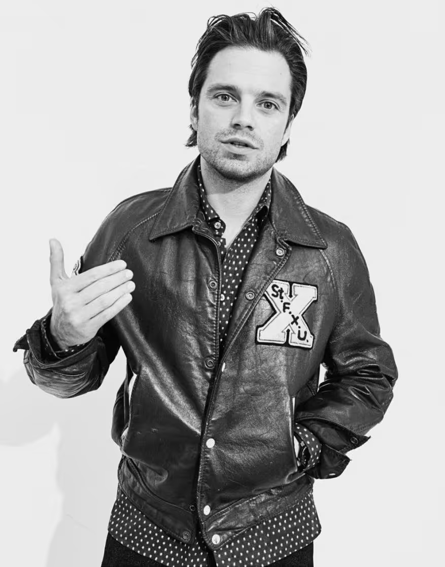 Black and white portrait of adult male in leather jacket and patterned shirt gesturing with his left hand in a studio setting.
