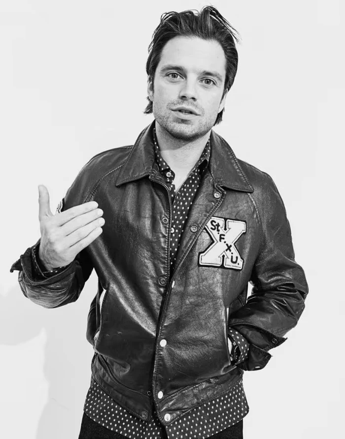 Sebastian Stan wearing a leather jacket and patterned shirt against a white backdrop