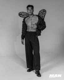 Man wearing butterfly wings and black trousers styled by Adam Ballheim against a grey seamless studio background.