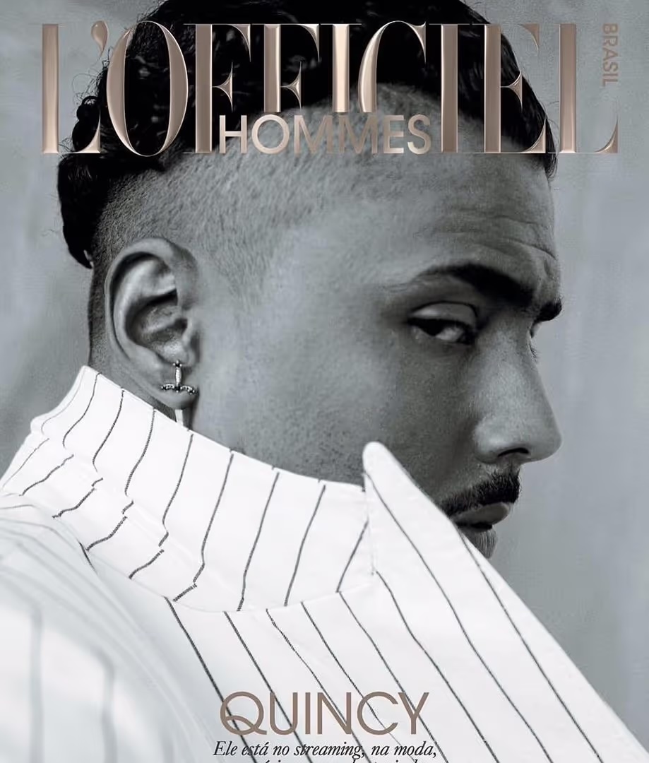 Black and white portrait of a man with an earring, wearing a striped shirt and a magazine cover with brand logo.