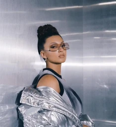 Portrait of a woman wearing futuristic tinted sunglasses, a black tank top, and a metallic silver puffer jacket