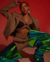 Woman in plaid blazer and matching trousers wearing metallic green boots against a red background.