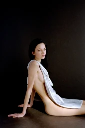 Model with dark hair draped in white fabric seated against a dark background