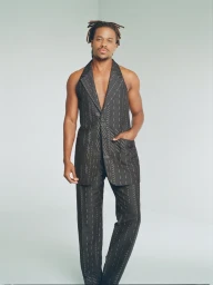 Man wearing a patterned sleeveless blazer and matching trousers standing against a plain white studio background.