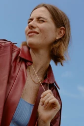 Low-angle portrait of a woman wearing a dark red leather jacket against a clear blue sky, styled by Ali Kornhauser
