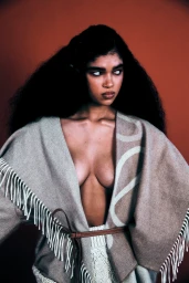 Portrait of a woman with long dark hair wearing a patterned beige poncho styled by Ali Kornhauser against a dark red backdrop