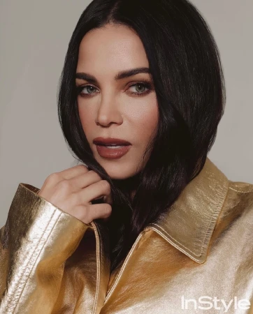 Close-up portrait of a woman with dark hair wearing a metallic gold jacket against a neutral studio background.