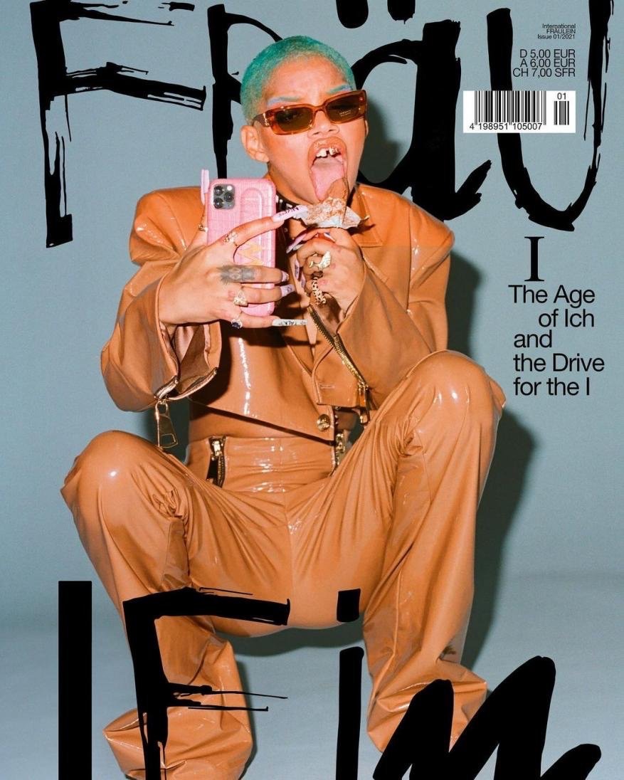 Magazine cover featuring a model with unique style, wearing sunglasses and holding a phone, against a pale blue background.