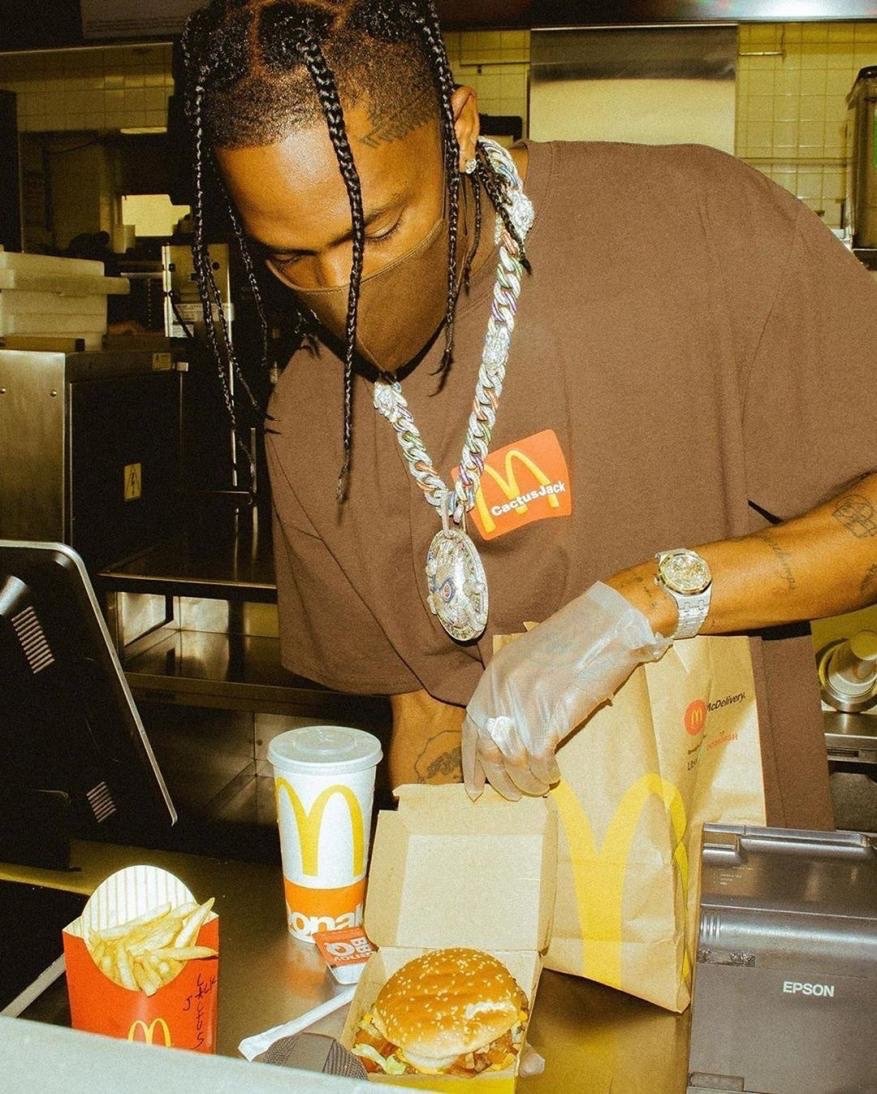 Travis Scott at McDonald's: Close-up of the rapper in a Cactus Jack brown shirt, mask, and iced-out chain, holding fast food.