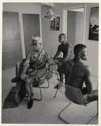 Monochrome portrait of a person in leopard print seated with two shirtless men in a modern interior