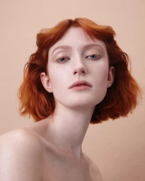 Portrait of a red-haired woman with blue eyes and light makeup against a warm solid backdrop