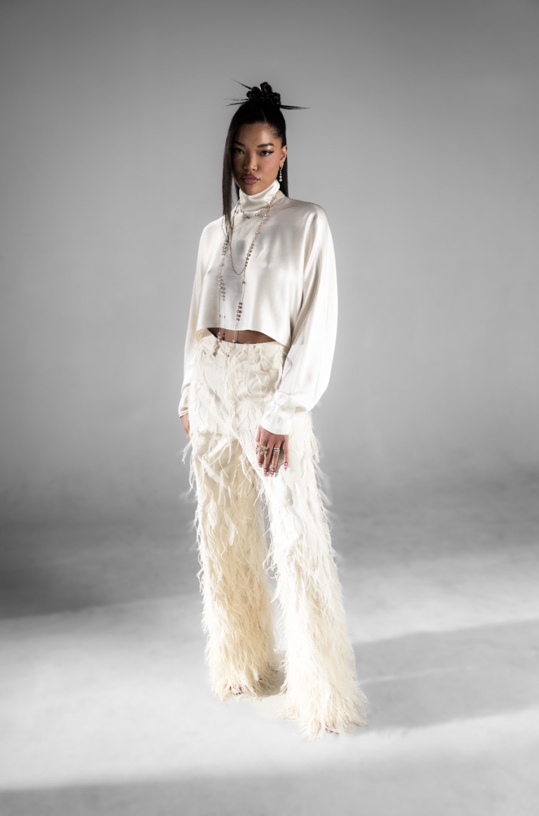 Elegant Asian woman in feathered pants and a silk top poses in a photo studio with soft, diffused lighting, showing off a unique fashion style.