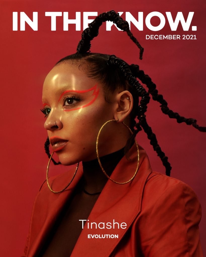 Magazine cover featuring Tinashe with bold red makeup, wearing a blazer and large gold hoop earrings, against a matching red background.