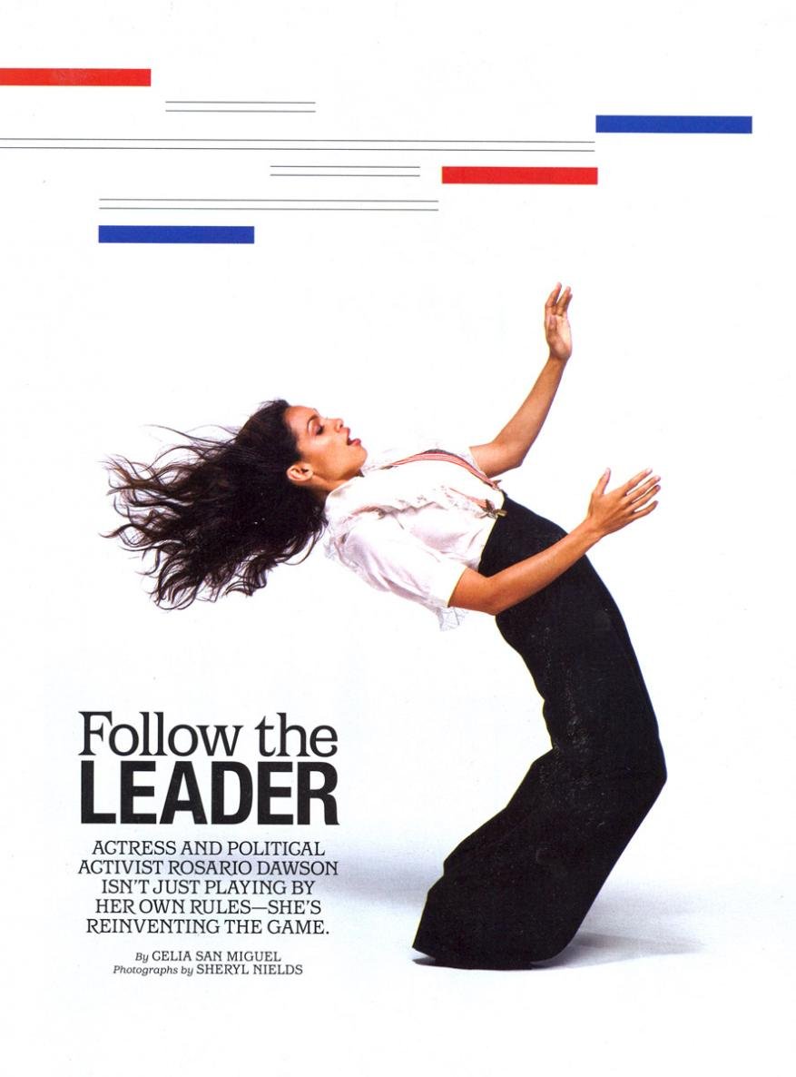 Rosario Dawson is featured in a fashion editorial, wearing dark trousers and a white blouse, set against a bright backdrop with linear graphics.