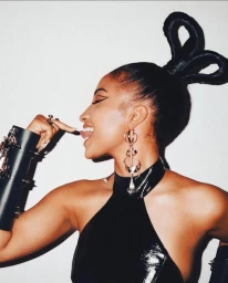 Profile view of a woman wearing a black halter top, sculptural updo, and metallic drop earrings against a plain background