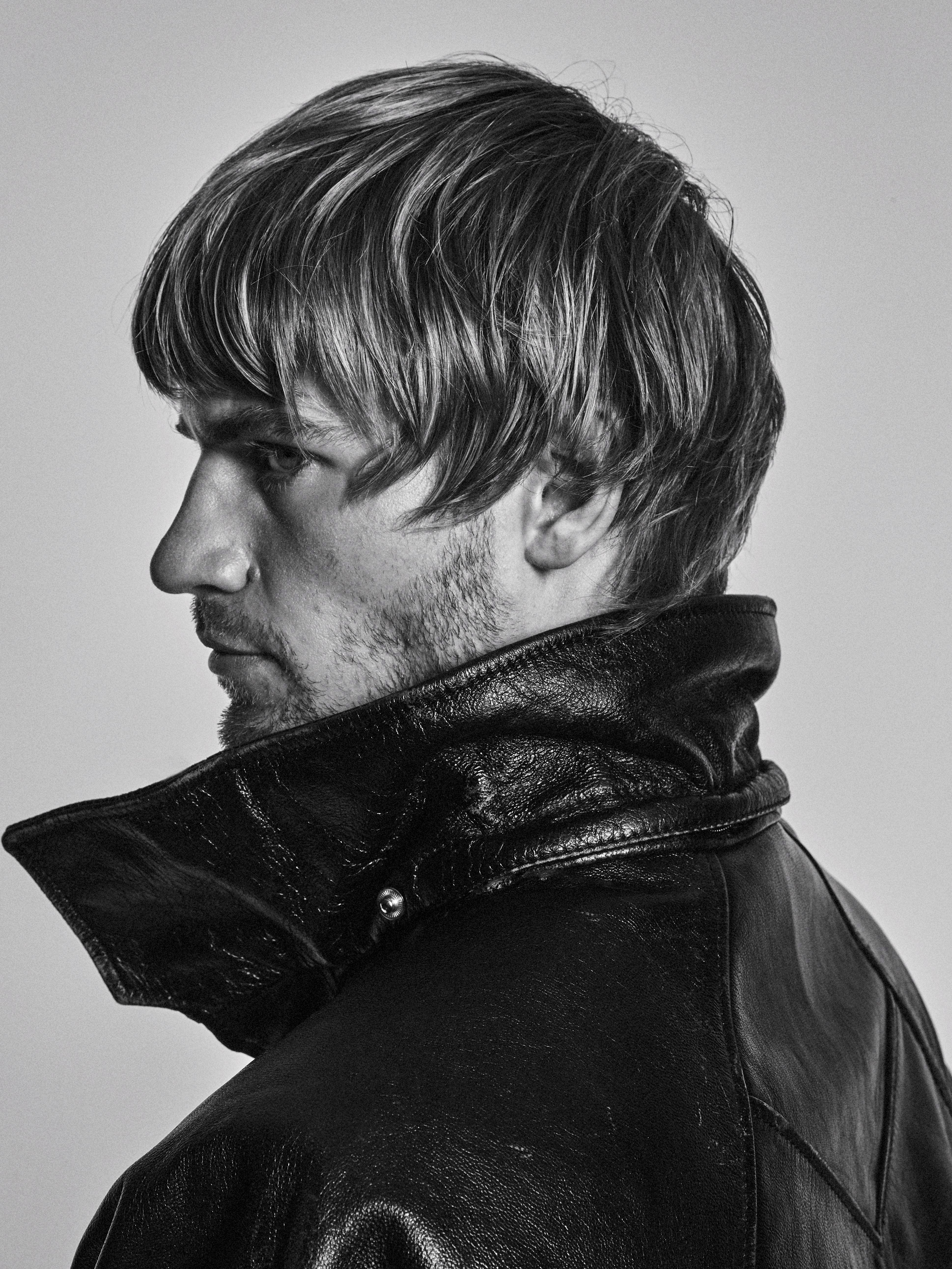 Black and white portrait of an adult male with blond hair and a beard wearing a black leather jacket against a neutral background.