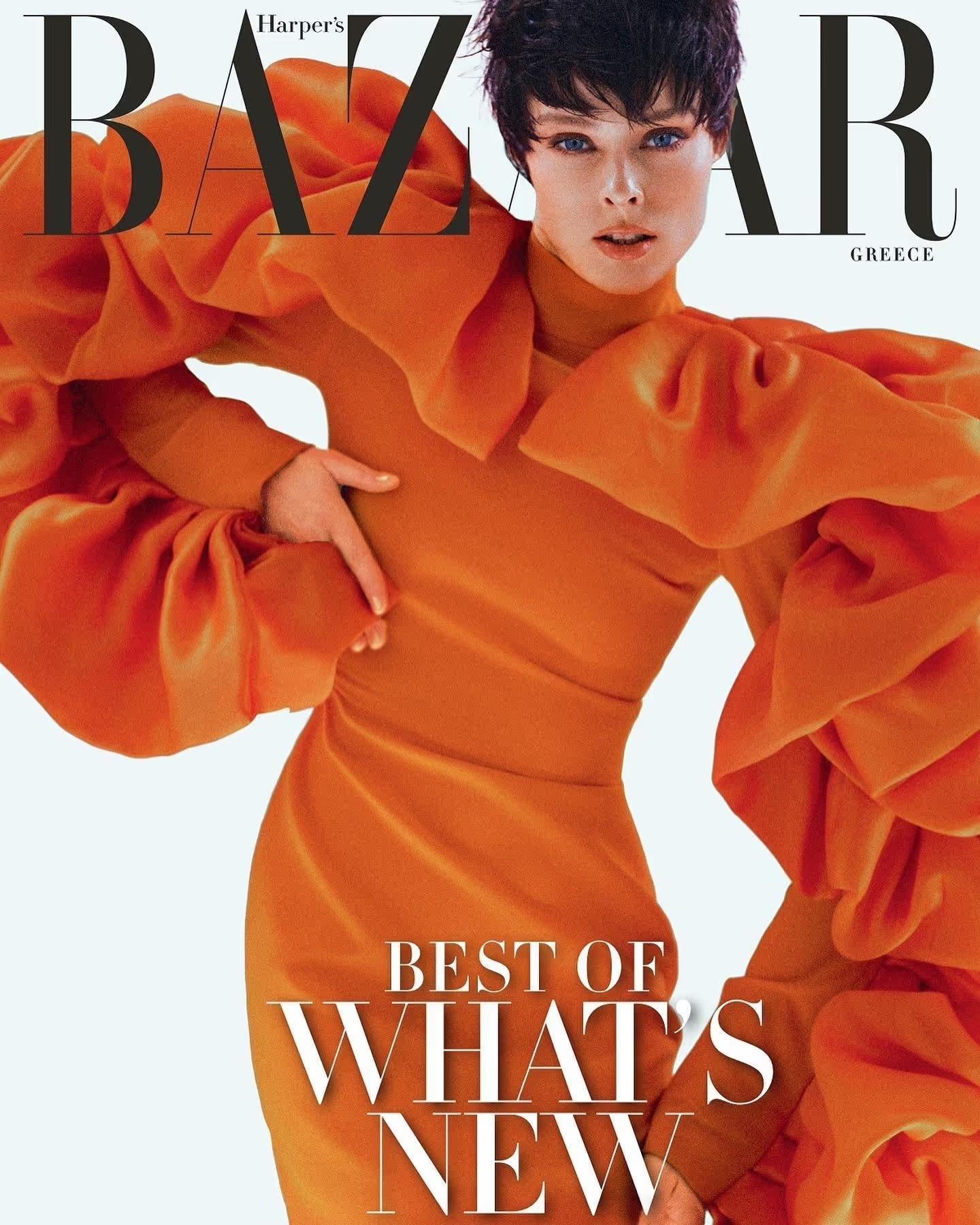 Magazine cover featuring a fashionable woman in a bright orange dress with ruffled sleeves against a clean white backdrop.