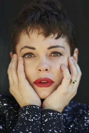 Close-up portrait of a woman with short dark hair, red lips, and both hands pressed against her cheeks.