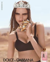 Model wearing a jeweled tiara and large statement rings holding hand near mouth against an arid outdoor background