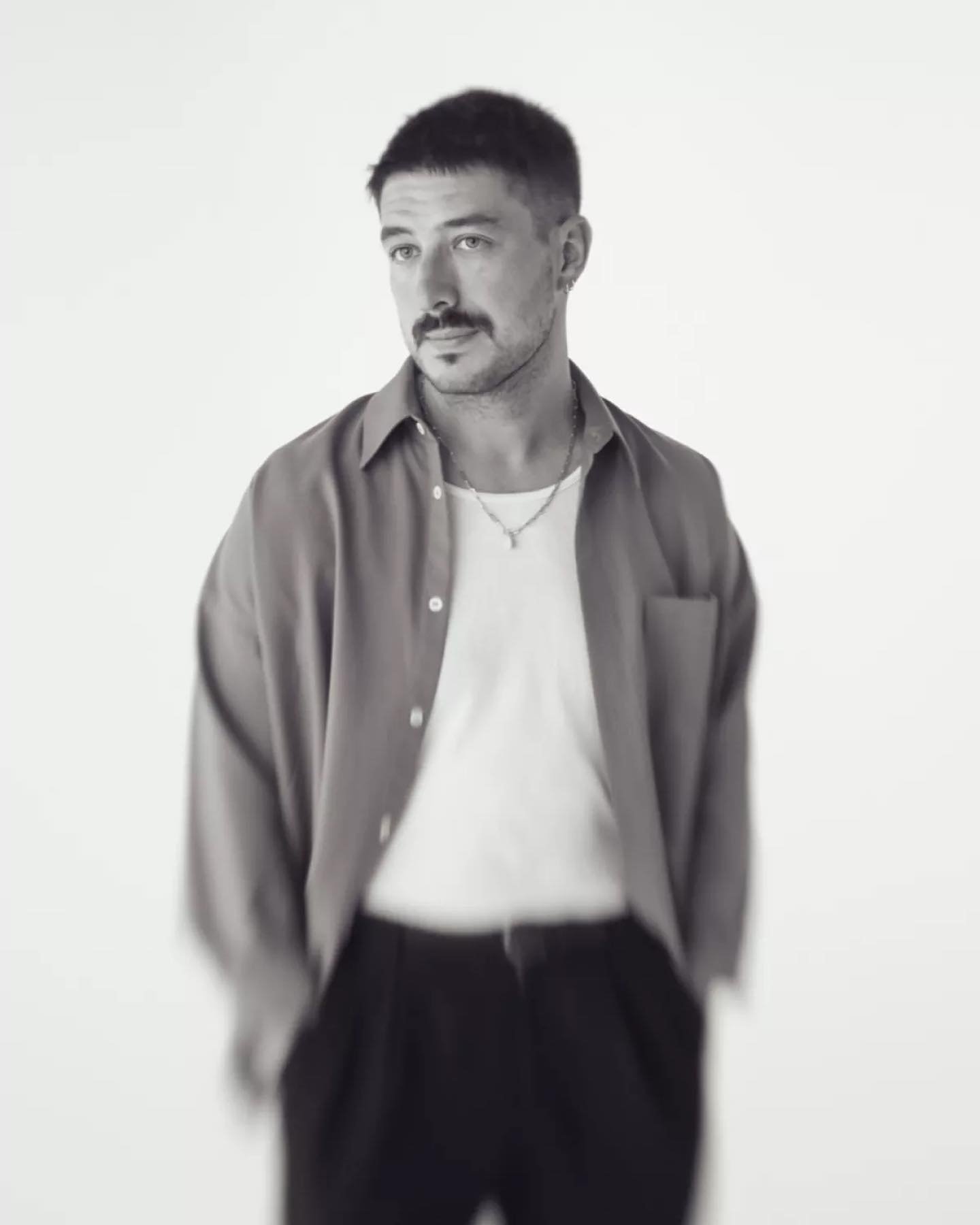 Monochrome portrait of a man wearing a button-down shirt and t-shirt, looking off-camera against a white background, minimalist aesthetic.