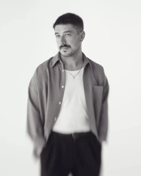 Portrait of a man with short hair and a mustache wearing an unbuttoned shirt over a white tank top