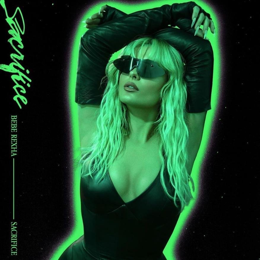 Bebe Rexha poses with a direct gaze and upturned head, highlighted by neon green lighting on a black background, for a promotional cover.