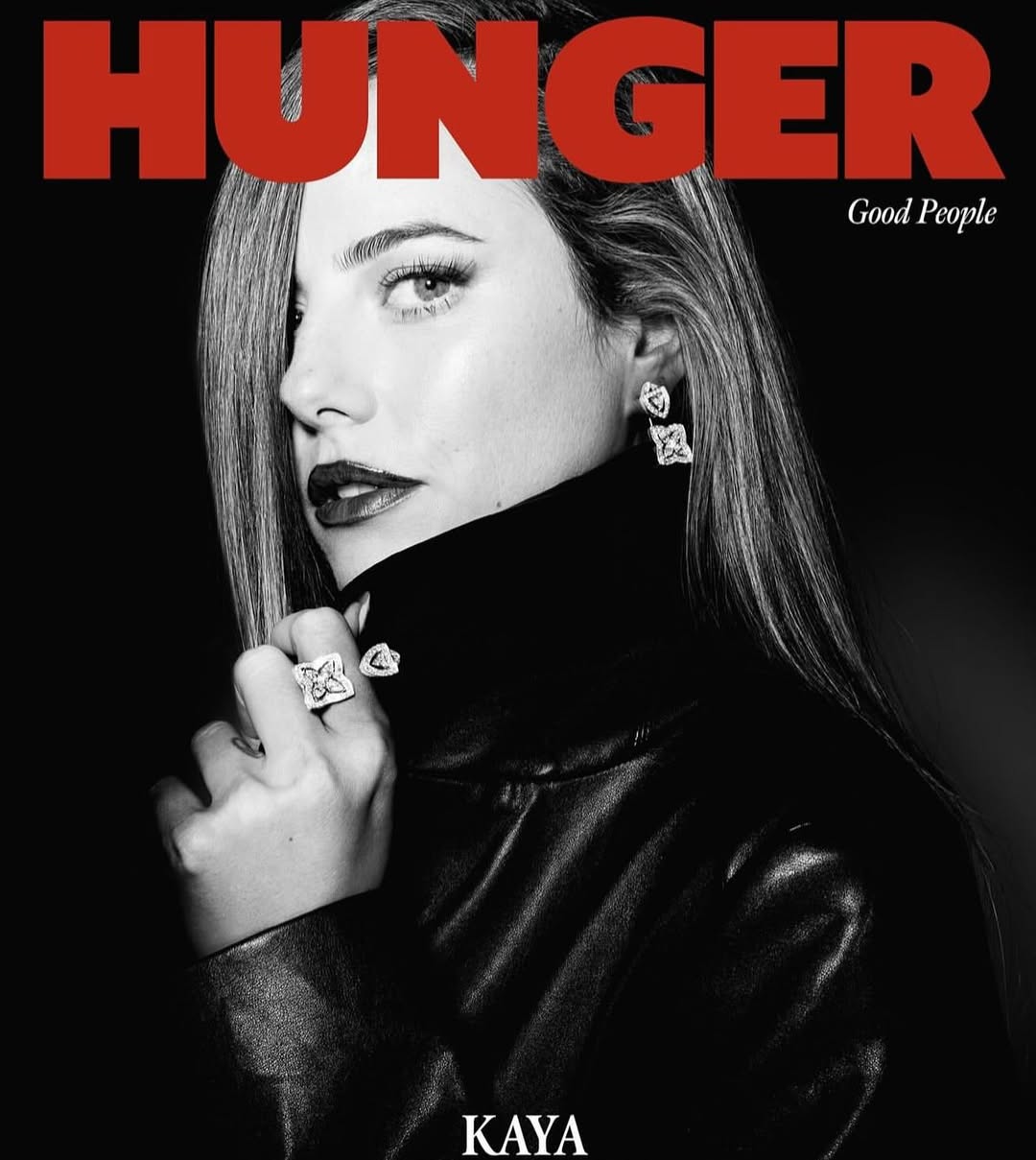 Black and white portrait of a female model wearing a black jacket, diamond earrings, and a ring against a black background.