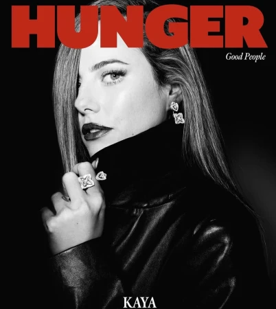 Black and white portrait of a female model wearing a black jacket, diamond earrings, and a ring against a black background.