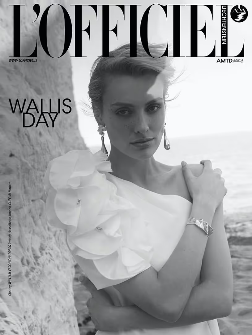 Black and white portrait of a woman in a white dress with a large floral detail, wearing earrings and a bracelet, posing outdoors.
