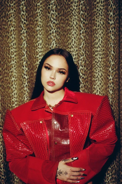 Portrait of a stylish young woman with black hair and a red jacket, posing indoors against a leopard-print background, in a fashion-forward setting.