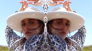 Mirrored image of a woman in a cowboy hat in a desert landscape with a light blue sky on a sunny day, shot in a medium shot.