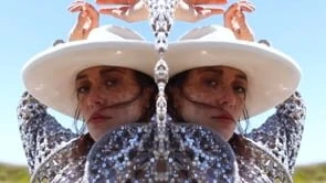 Mirrored image of a woman in a cowboy hat in a desert landscape with a light blue sky on a sunny day, shot in a medium shot.