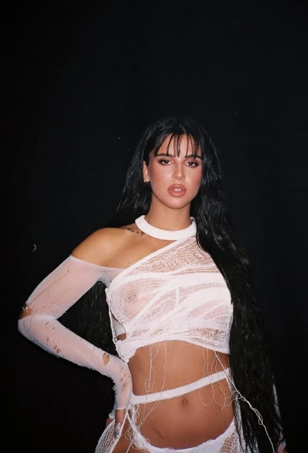 Brunette woman in white mesh fashion outfit against a black background, posing for a portrait in a photo studio.