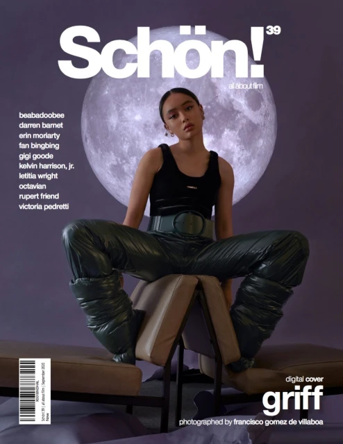 Magazine cover featuring a woman in a black top and shiny green pants, seated on a prop with a moon backdrop, promoting Schon!