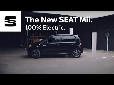 Black SEAT Mii electric car showcased indoors in a studio, accompanied by branding elements and a charging station.