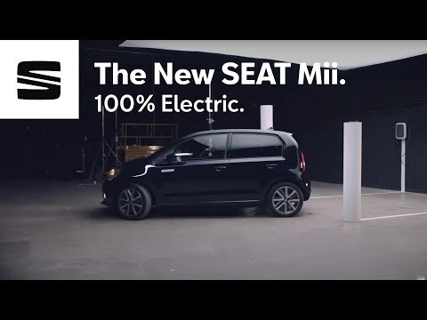 Black SEAT Mii electric car showcased indoors in a studio, accompanied by branding elements and a charging station.