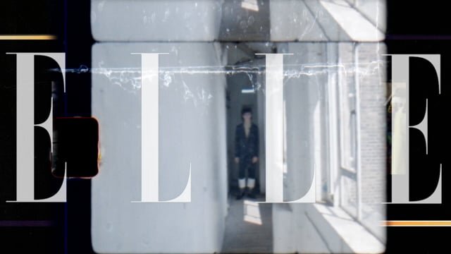 Editorial shot with a person in a hallway framed by the 'ELLE' logo. The color palette includes grays, whites, and blacks.