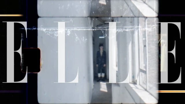 Editorial shot with a person in a hallway framed by the 'ELLE' logo. The color palette includes grays, whites, and blacks.