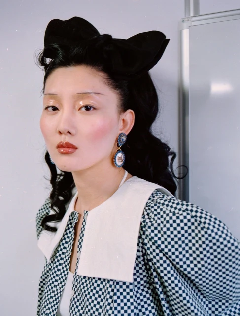 Headshot of an Asian woman wearing a black-and-white checkered jacket with a white collar and a large black bow in her hair.
