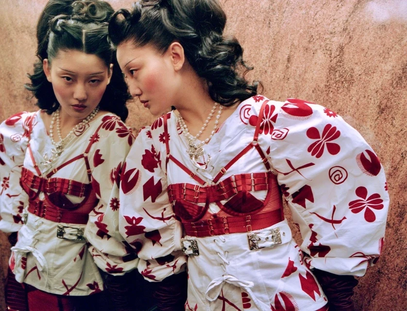 Artistic portrait of an Asian woman with styled hair and a patterned top, reflected in a mirror, in a fashion or beauty context.