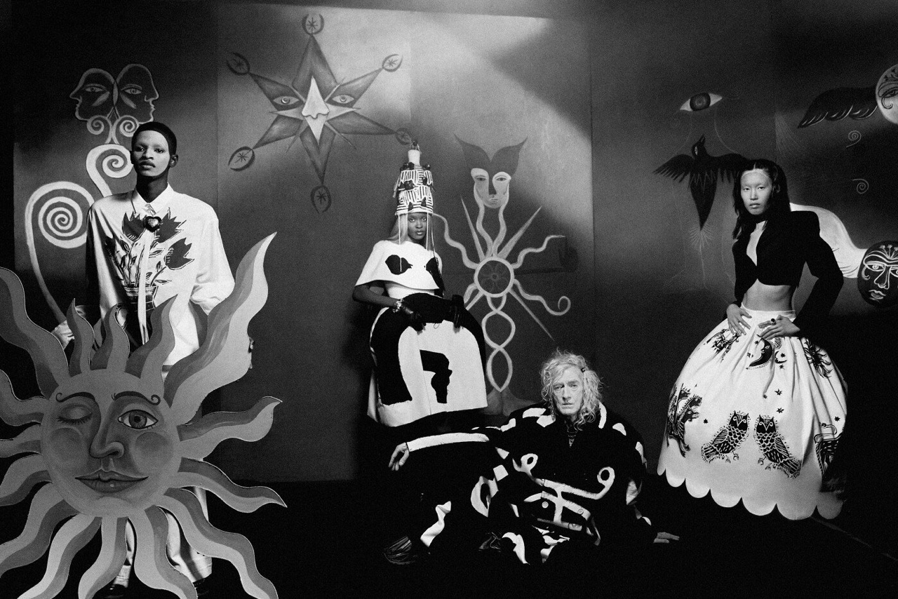 Monochrome studio shot of four models in black and white clothing with stylized graphic designs posing in front of hand-painted backdrop.